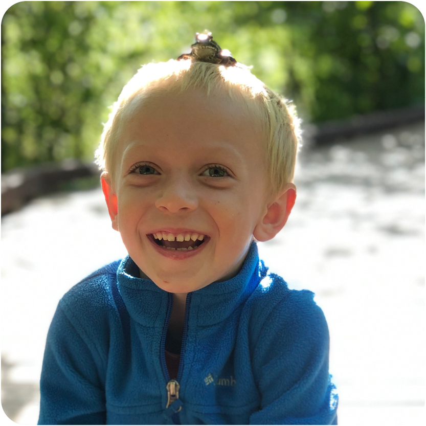 Young boy sitting with a frog on his head and laughing outside