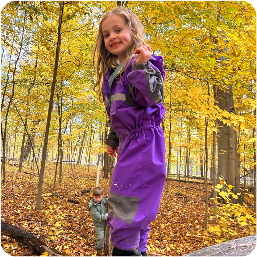 Young girl smiling and playing on logs outside in the woods