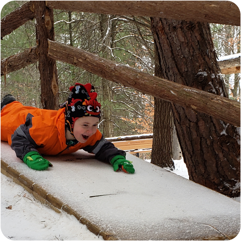 Young boy playing in the snow sliding down a ramp outside in the woods