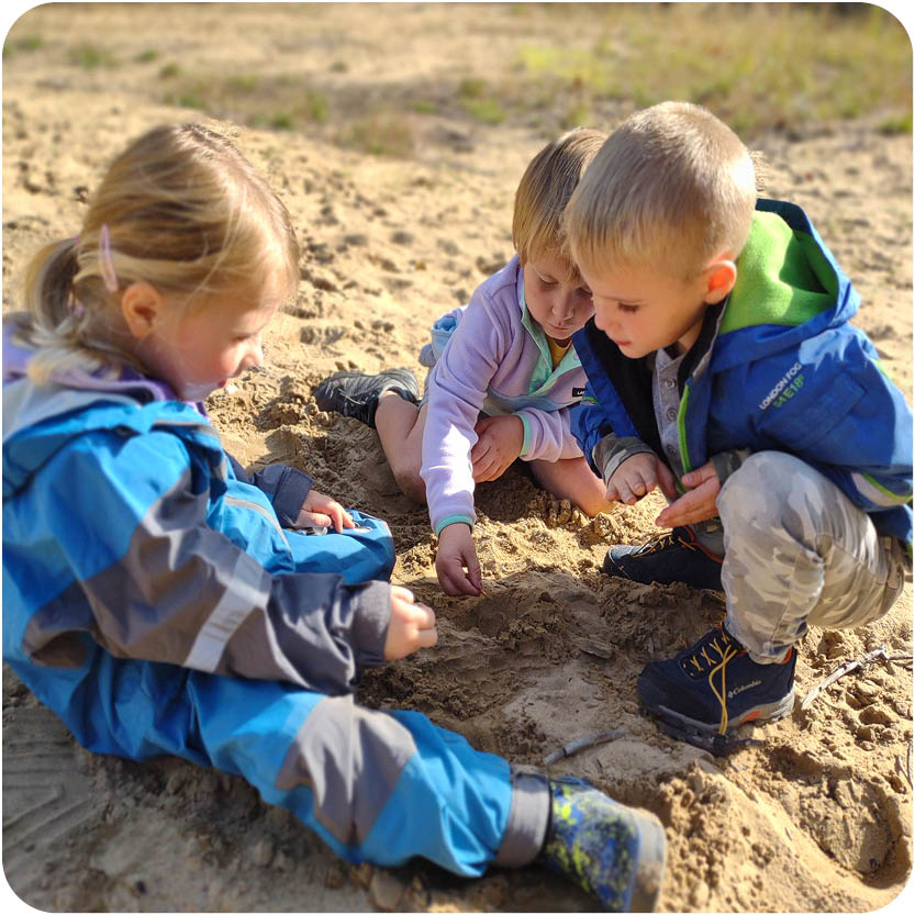 Three kids playing in sandy area discovering nature